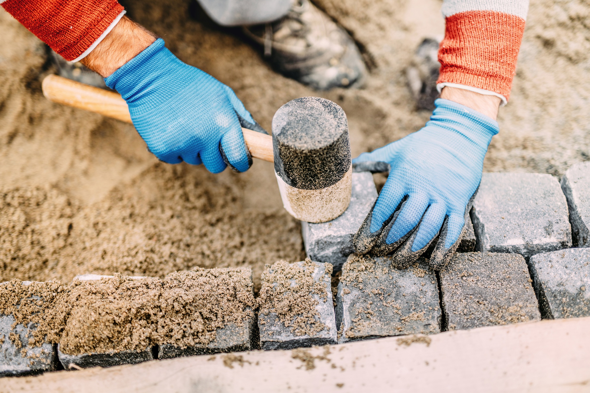 Construction worker placing stone tiles, cobblestone blocks in s